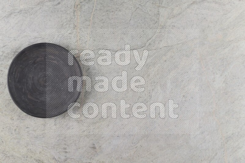 A circular black pottery plate on grey marble background