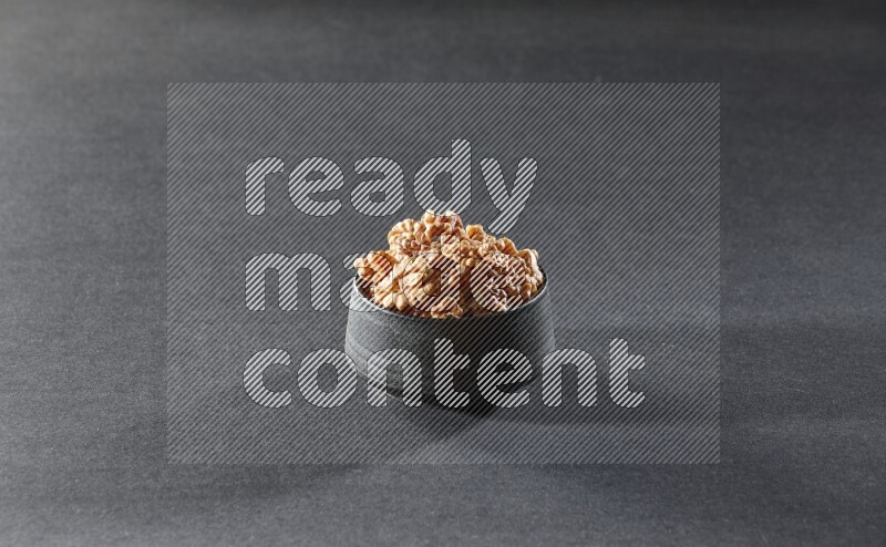 A black pottery bowl full of peeled walnuts on a black background in different angles