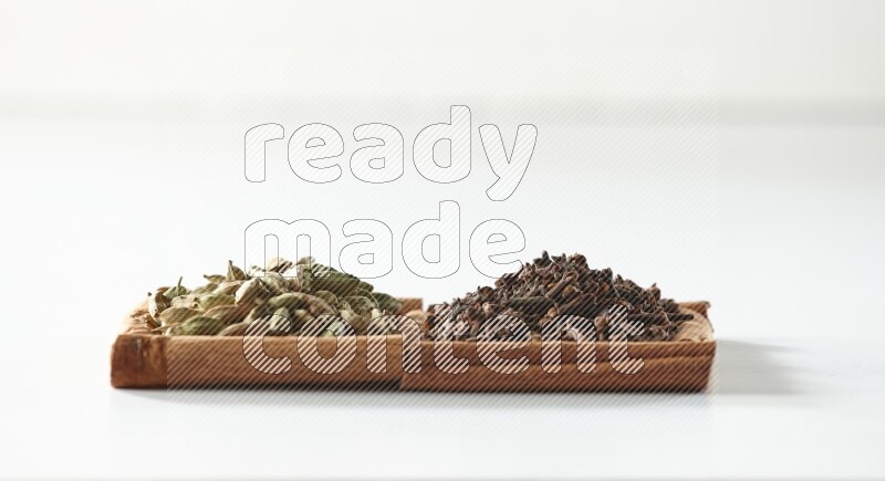 مربعان من أعواد القرفة ممتلئان بالقرنفل وحبوب الهيل علي خلفية بيضاء