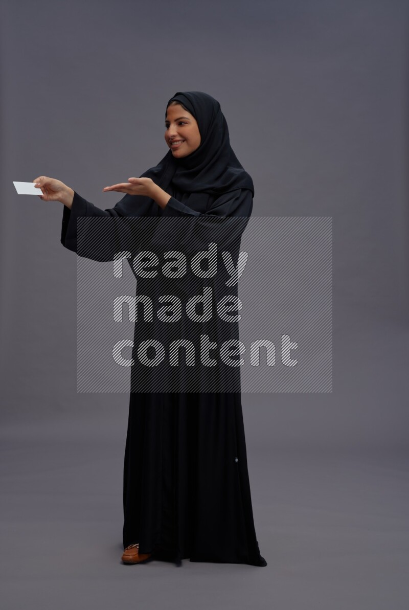 Saudi woman wearing Abaya standing holding ATM card on gray background