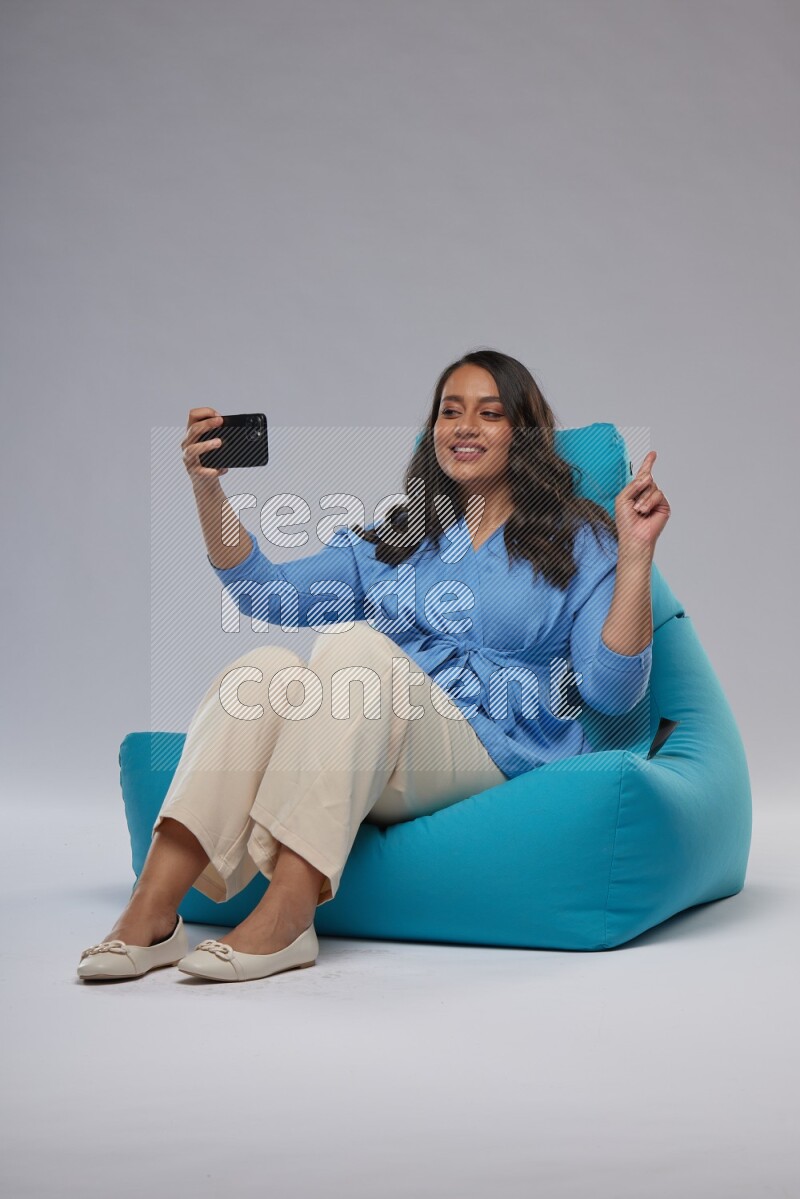 A woman sitting on a blue beanbag and taking selfie