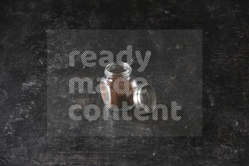 وعاء بهارات زجاجي ممتلئ ببودرة القرنفل على أرضية سوداء