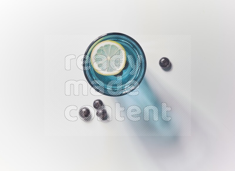 Blue transparent glass filled with blueberries decorated with lemon slices on a white background