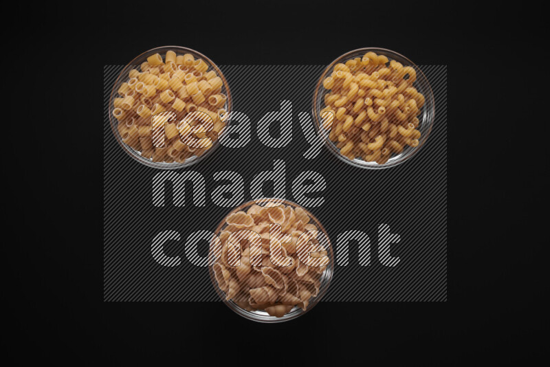Different pasta types in glass bowls on black background