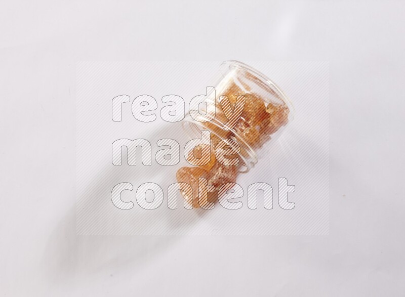 وعاء زجاجي ممتلئ بقطع الصمغ العربي والوعاء مقلوب وبعض القطع متناثرة خارجه علي خلفية بيضاء