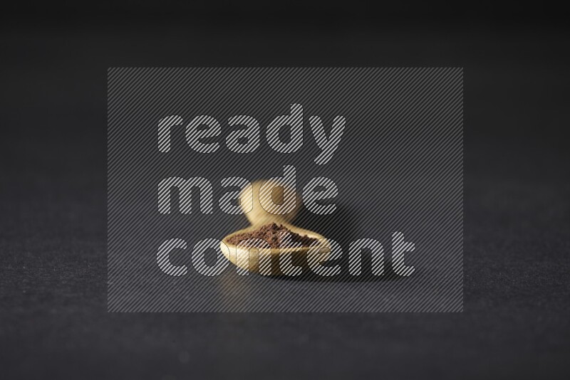 A wooden spoon full of cloves powder on a black flooring