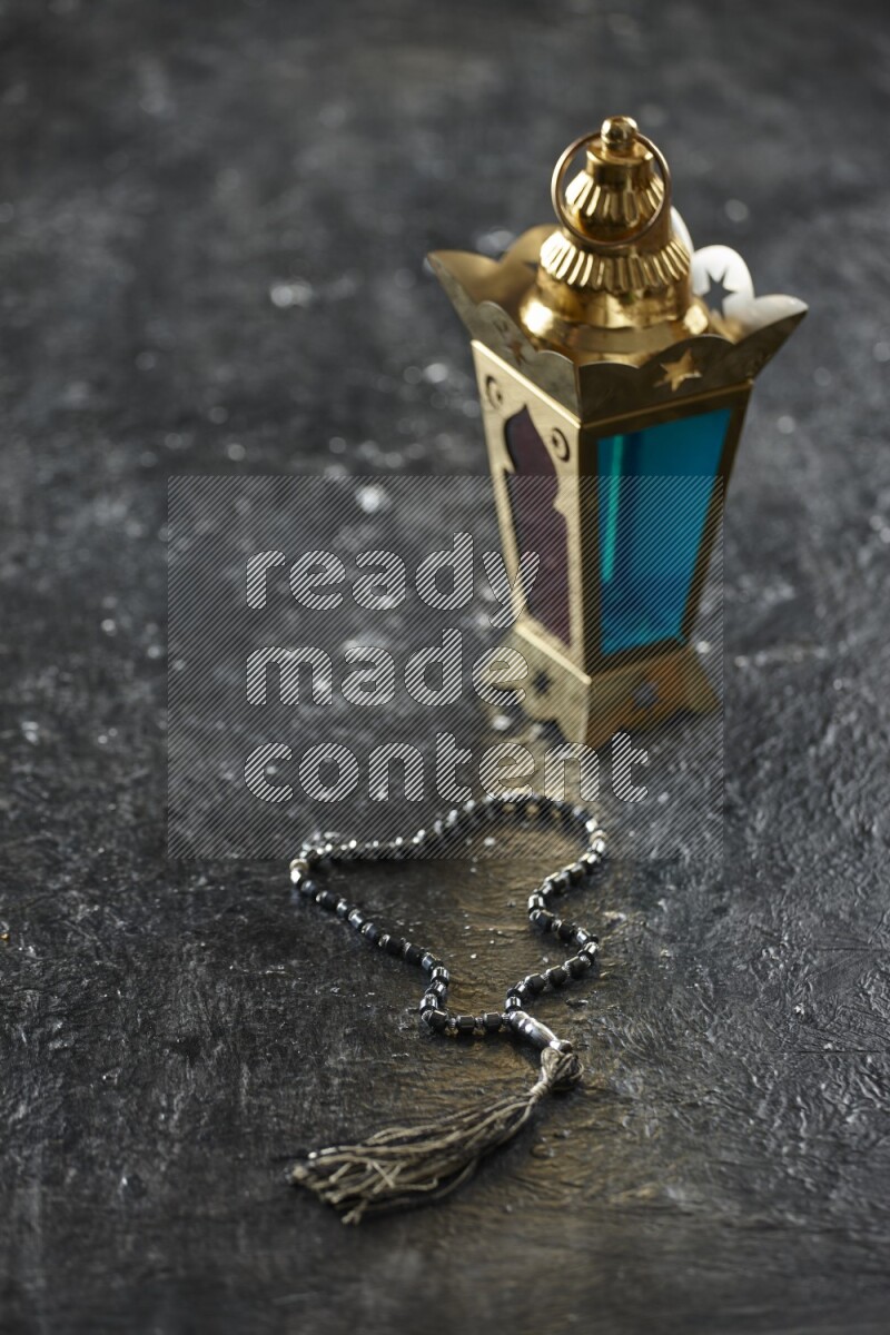 A golden lantern with different drinks, dates, nuts, prayer beads and quran on textured black background