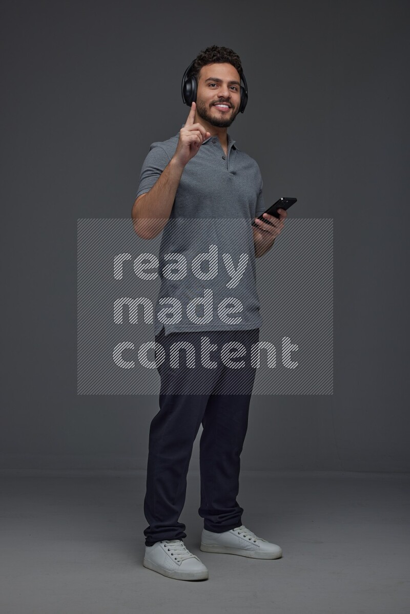 A man wearing casual and using his phone and headphone eye level on a gray background