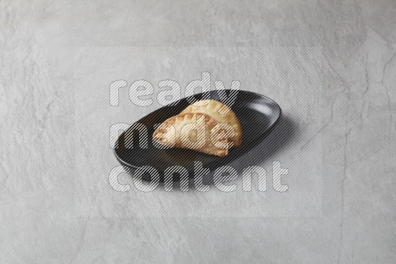Two fried sambosas in an oval shaped black plate on a gray background