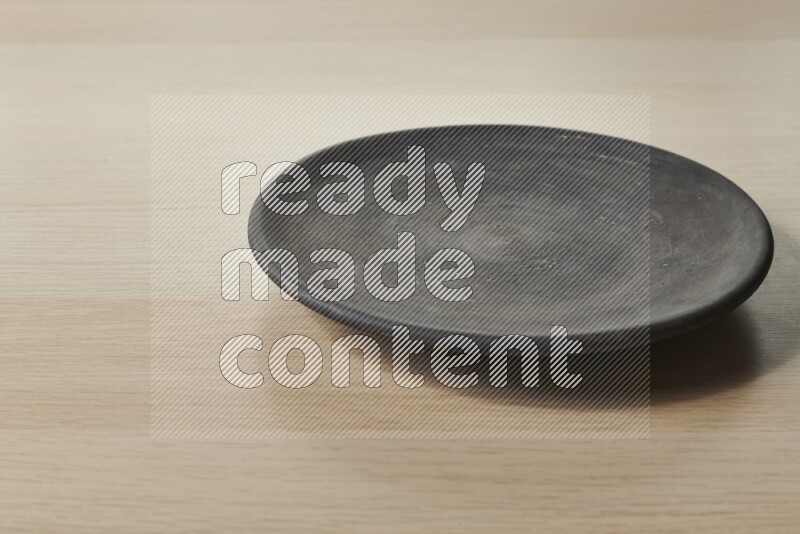 A circular black pottery plate on light wooden background