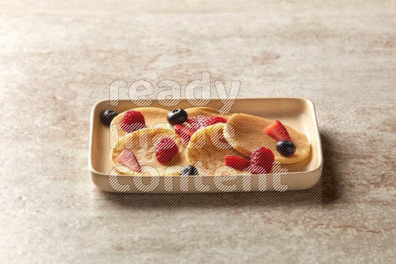 Five stacked mixed berries mini pancakes in a rectangular plate on beige background