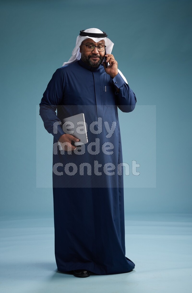 Saudi Man with shimag Standing talking on phone on blue background