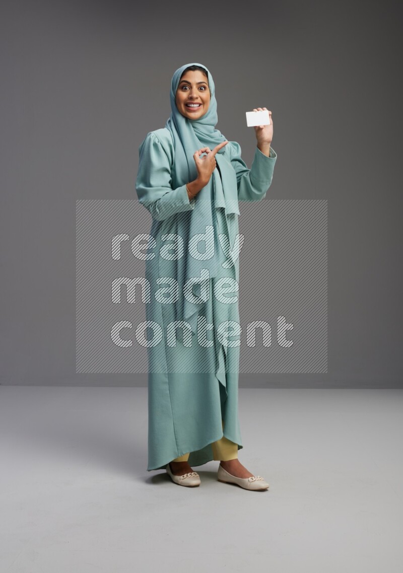 Saudi Woman wearing Abaya standing holding ATM card on Gray background