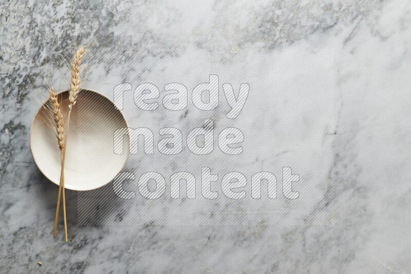Wheat stalks on beige pottery plate on grey marble background