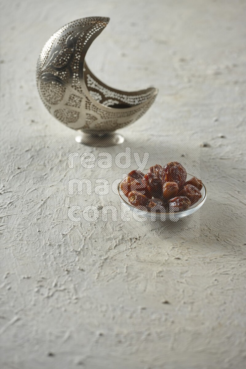 A silver lantern with different drinks, dates, nuts, prayer beads and quran on textured white background