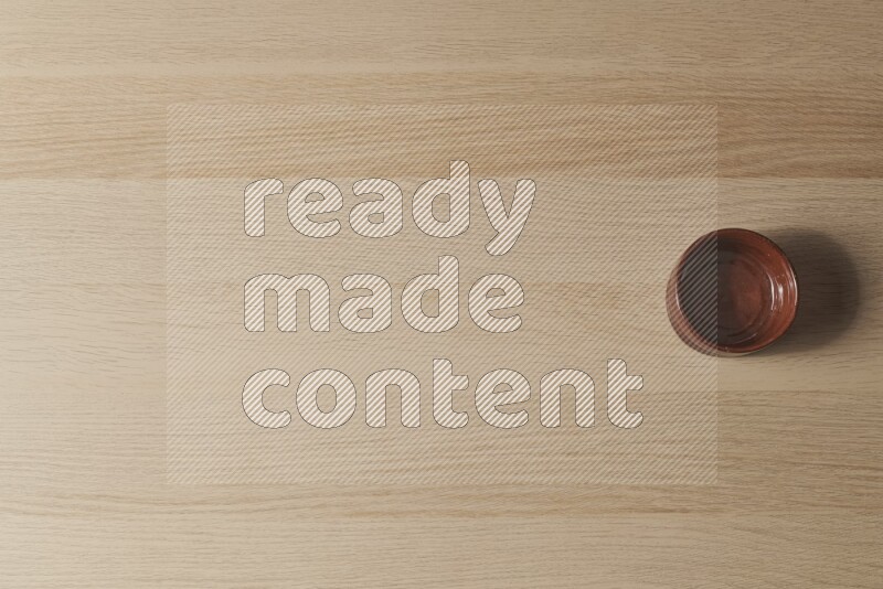 A brown pottery bowl on light wooden background