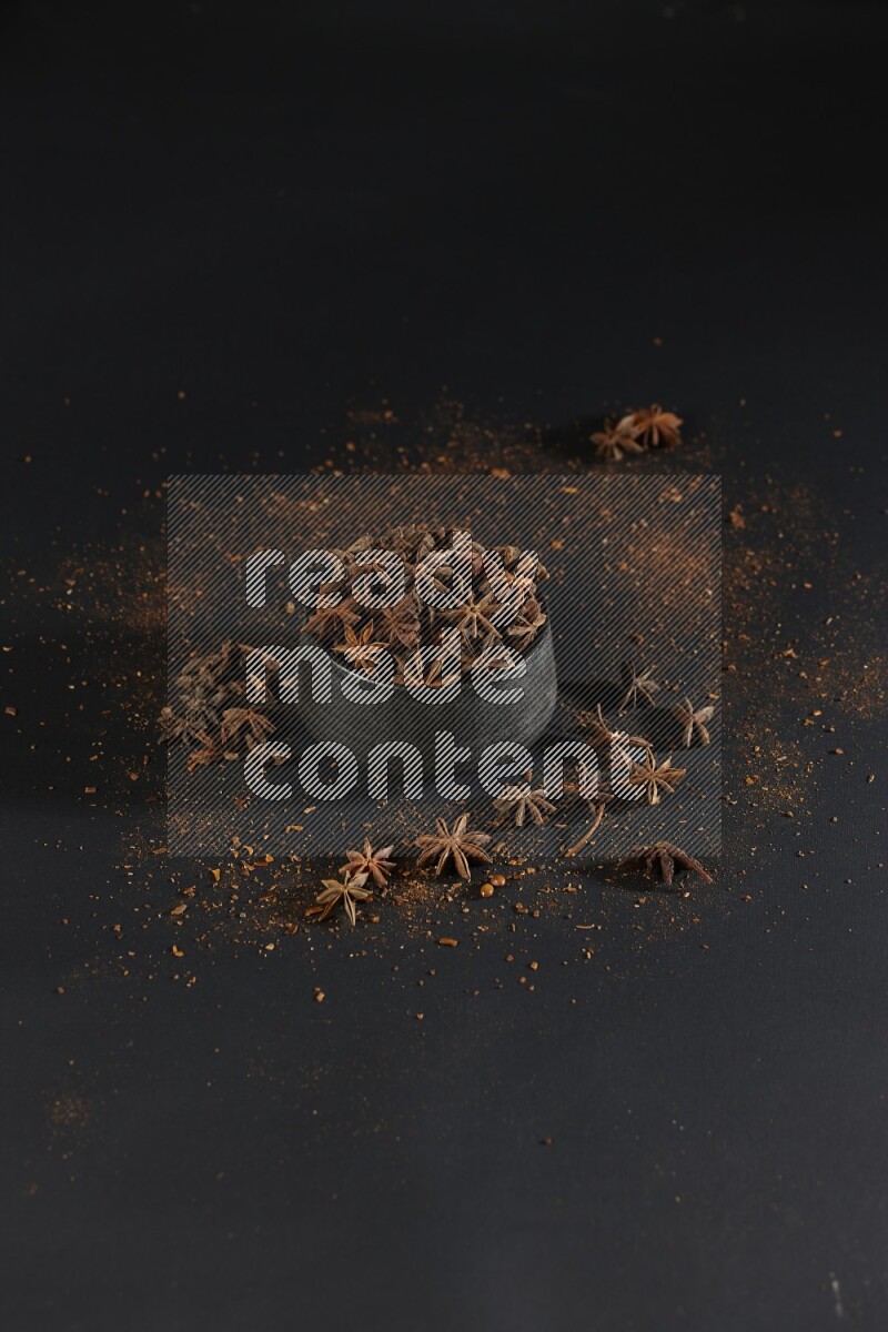Star Anise in a black bowl with sprinkled anise on black flooring
