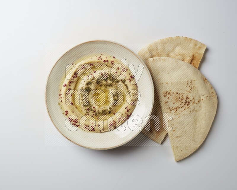 Hummus in a pottry plate garnished with zaatr & sumak on a white background