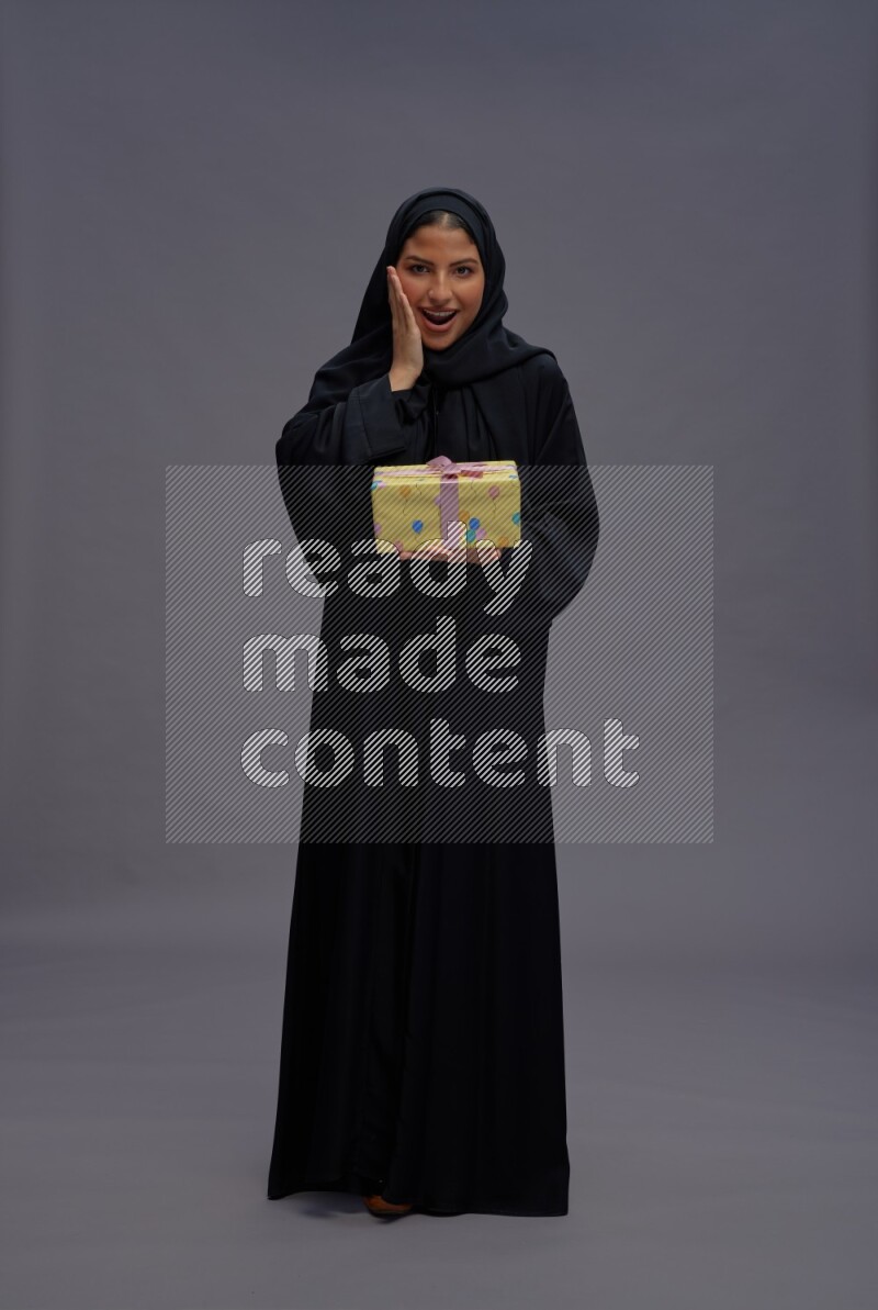 Saudi woman wearing Abaya standing holding gift box on gray background
