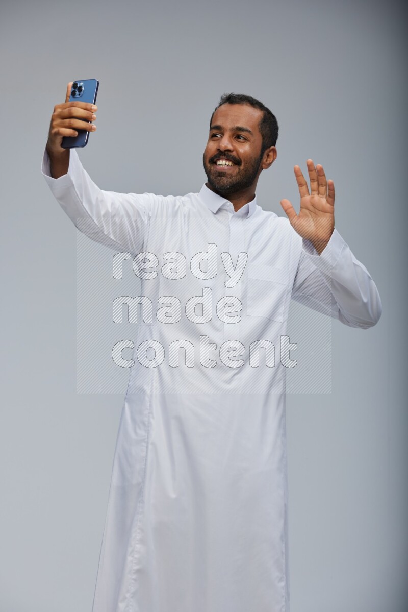 Saudi man wearing Thob standing taking selfie on Gray background