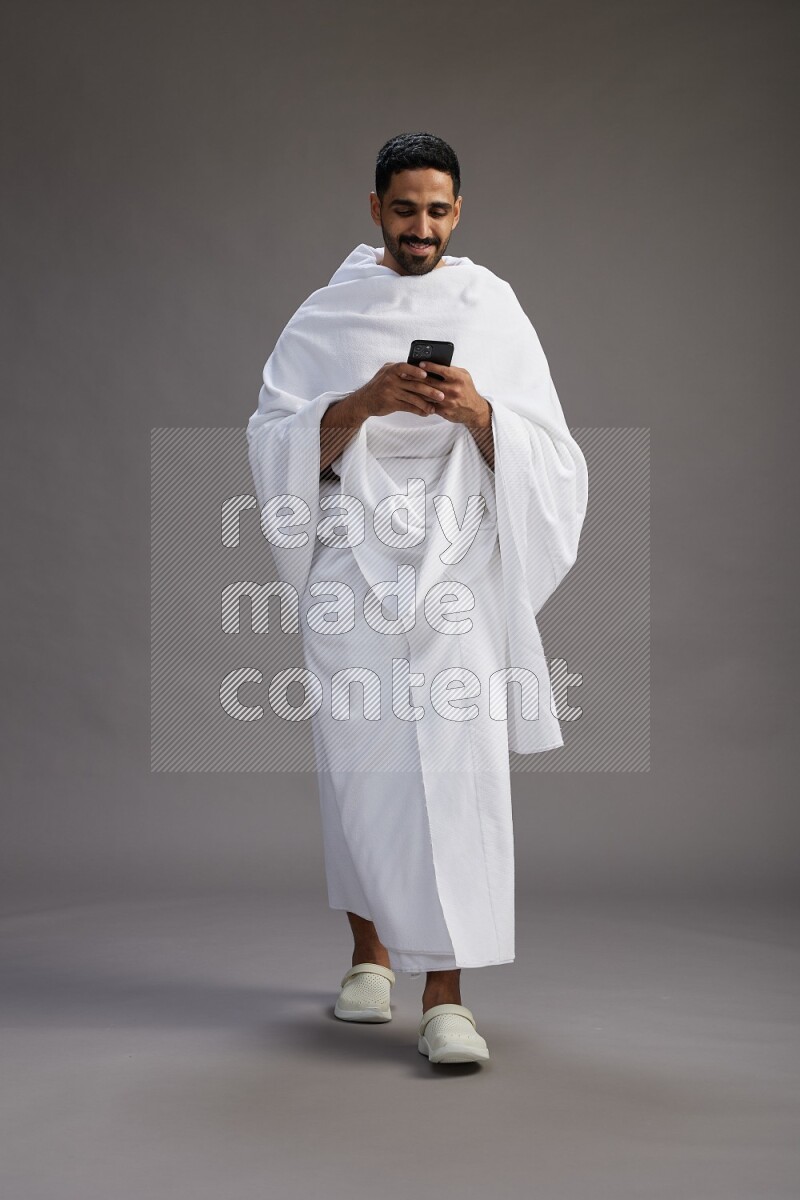 A man wearing Ehram Standing texting on phone on gray background