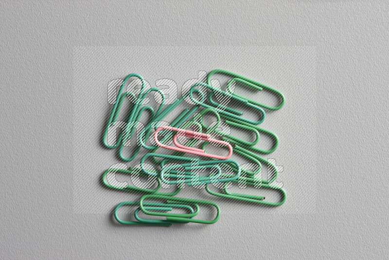 A bunch of green paper clips with a different colored paper clip in the center on grey background