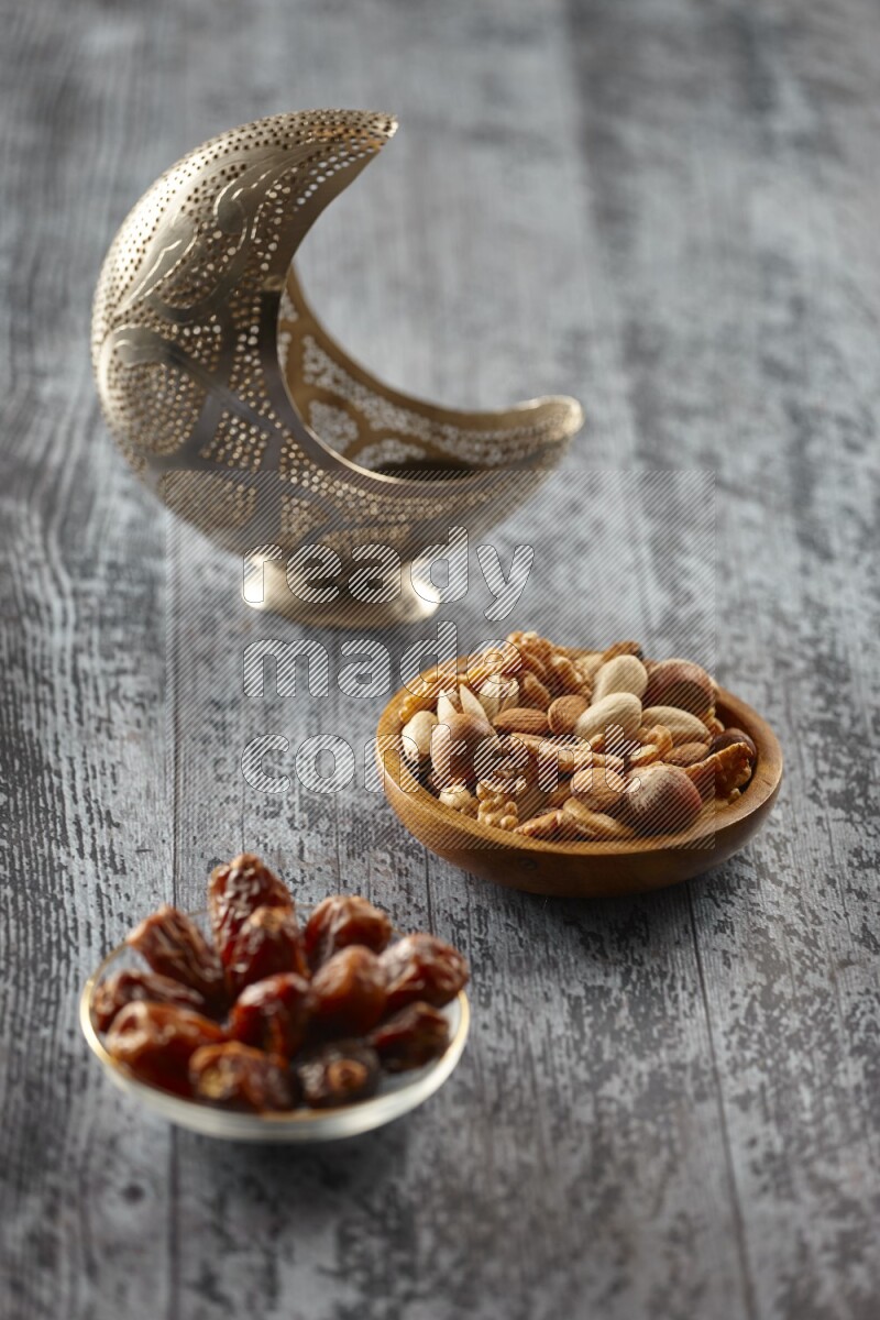 A silver lantern with different drinks, dates, nuts, prayer beads and quran on grey wooden background