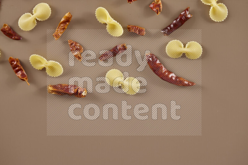 Raw pasta with different ingredients such as cherry tomatoes, garlic, onions, red chilis, black pepper, white pepper, bay laurel leaves, rosemary and cardamom on beige background