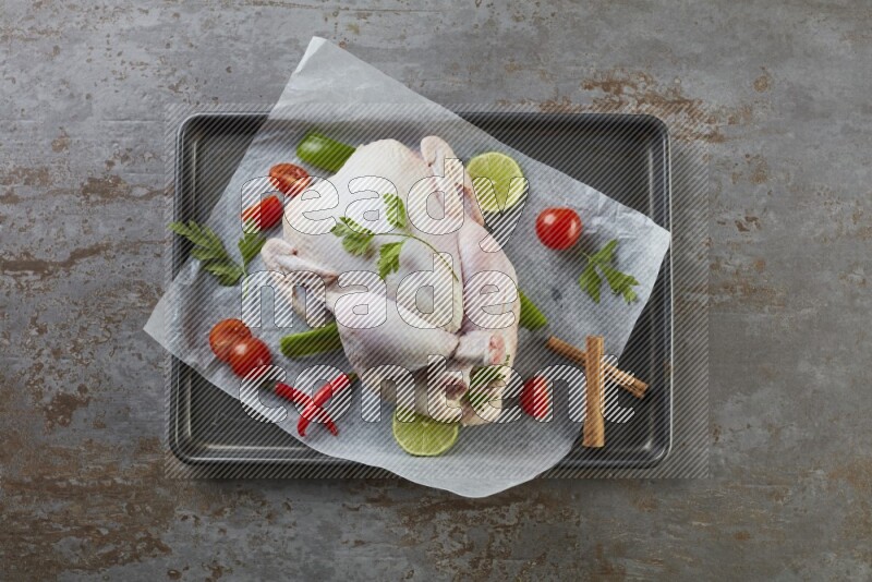 whole raw chicken on an oven trey direct on a rustic grey background
