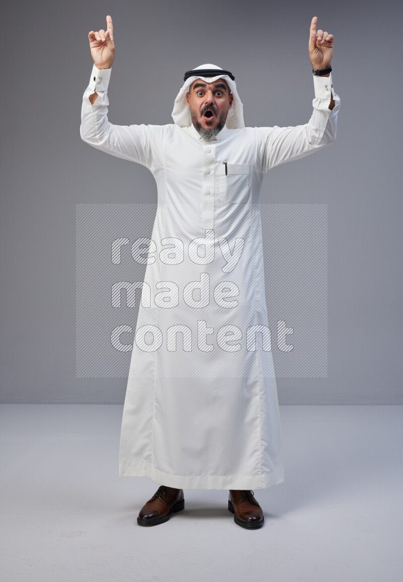 Saudi man Wearing Thob and white Shomag standing interacting with the camera on Gray background