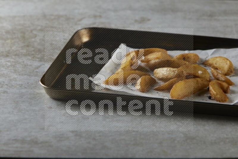 wedges potato on parchment paper in a black stainless steel rectangle tray on grey textured counter top