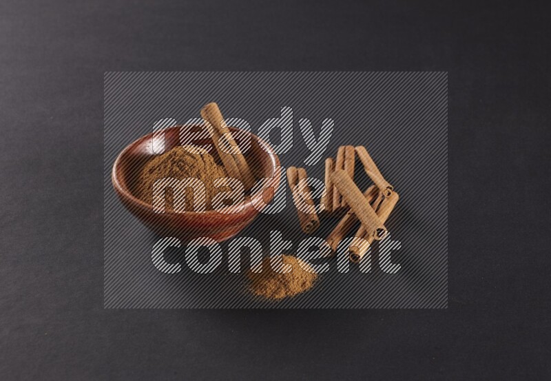 Cinnamon powder in a wooden bowl with a cinnamon sticks on black background
