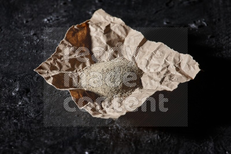 White pepper powder in a crumpled paper on textured black flooring