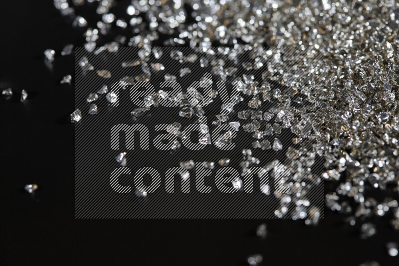 Silver shimmering fragments of glass scattered on a black background