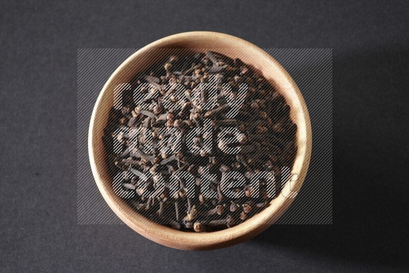 A wooden bowl full of cloves on a black flooring