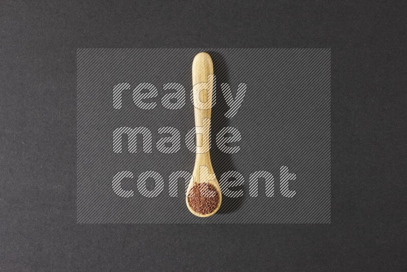 A wooden spoon full of garden cress seeds on a black flooring