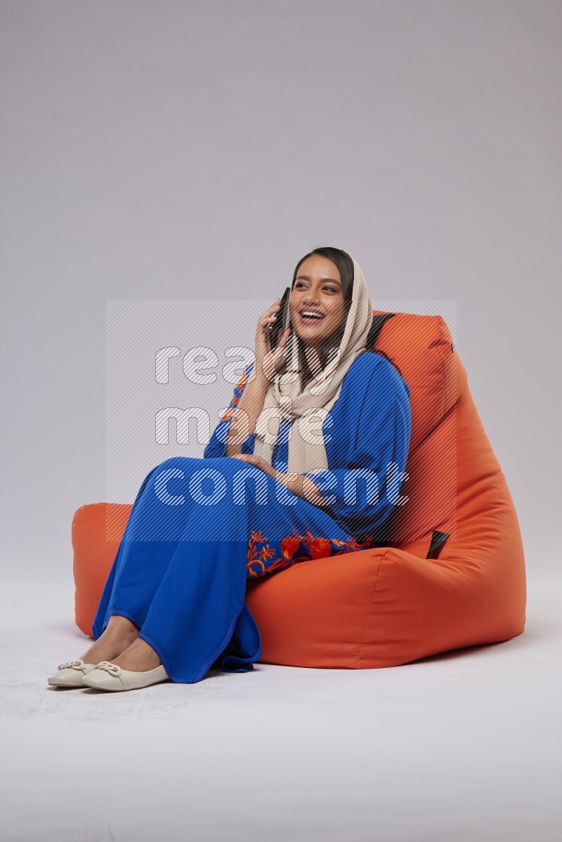 A Saudi woman wearing Jalabiya sitting on an orange beanbag and talking on the phone