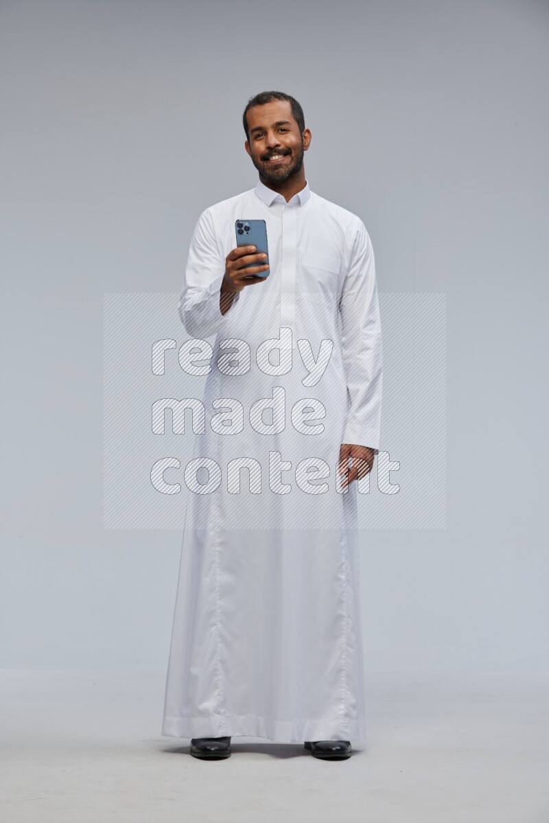 Saudi man wearing Thob standing texting on phone on Gray background