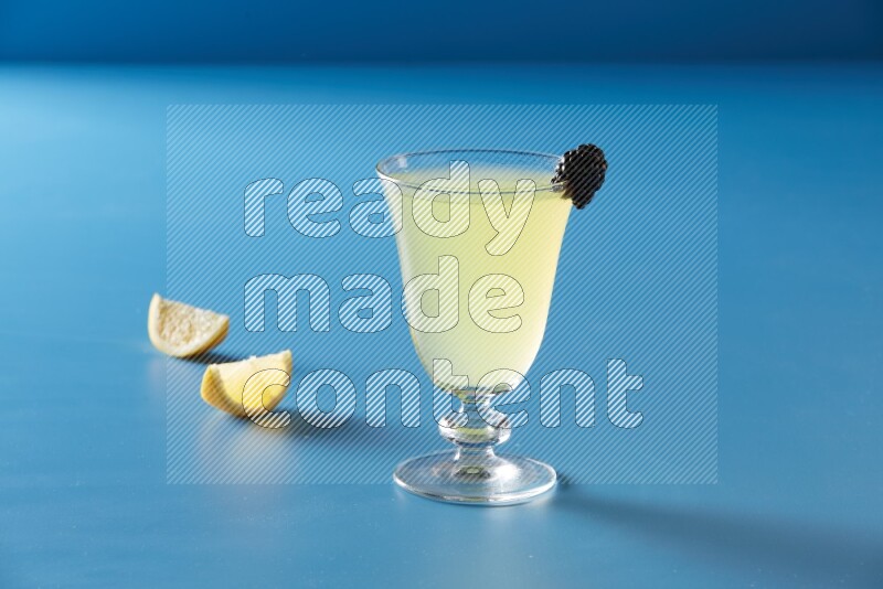 glass of lemon juice with berry on blue background