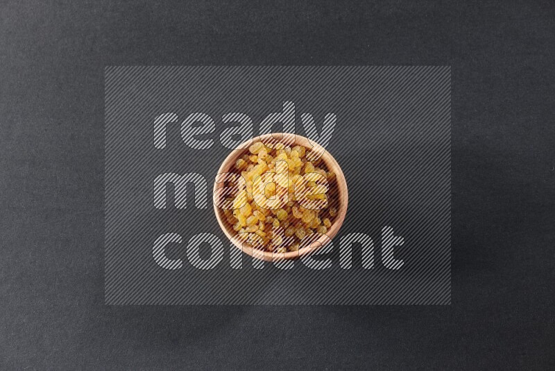 A wooden bowl full of raisins on a black background in different angles
