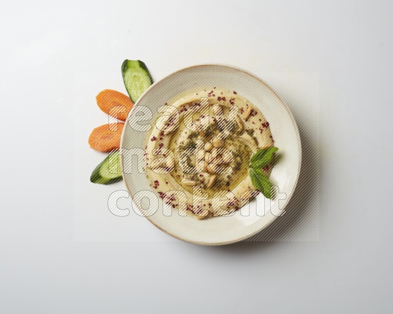 Hummus in a pottry plate garnished with zaatr & sumak on a white background