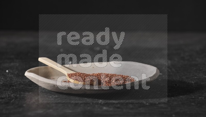 طبق فخار متعدد الألوان ممتلئ ببذور حب الرشاد وملعقة خشبية ممتلئة بالبذور على أرضية سوداء