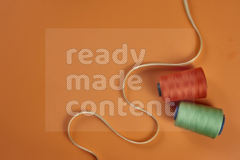 A green and orange collection of sewing and tailoring tools arranged on a orange background