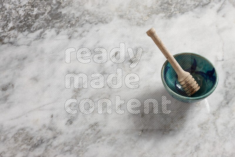 Decorative pottery bowl with wooden honey dipper in it on grey marble background