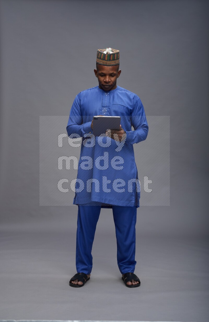 Man wearing Nigerian outfit standing working on tablet on gray background