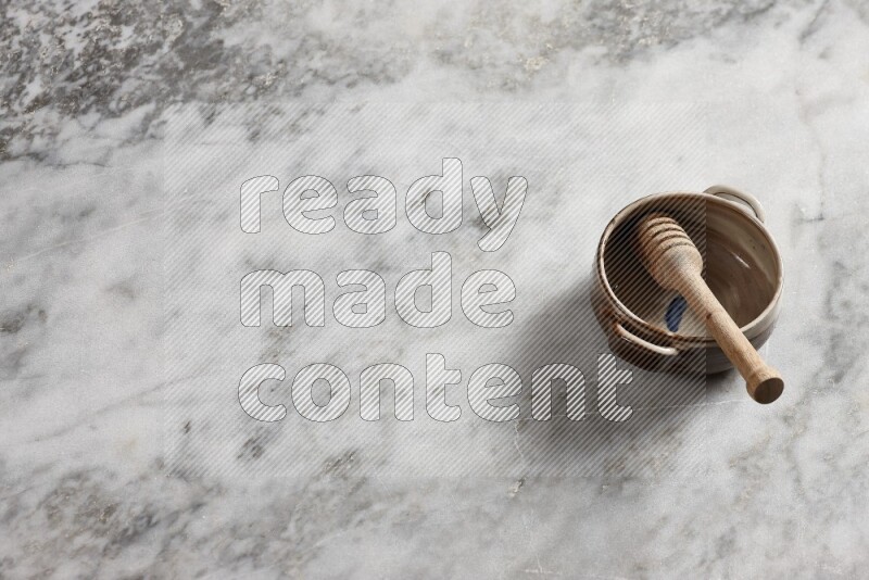 Multicolored pottery bowl with wooden honey dipper in it on grey marble background