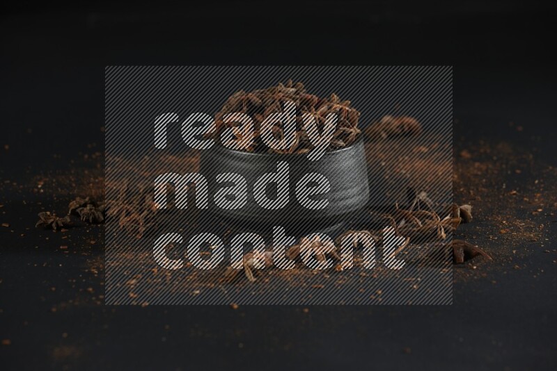 Star Anise in a black bowl with sprinkled anise on black flooring