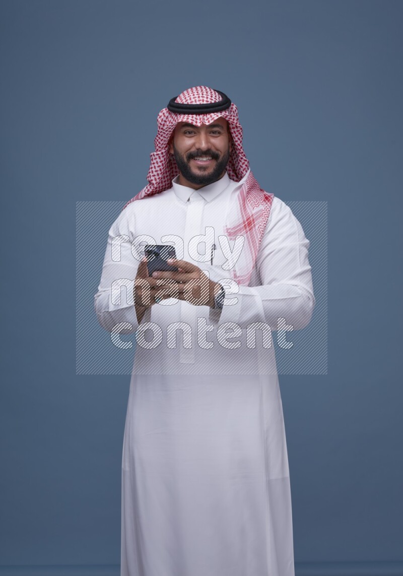 A man Texting on Blue Background wearing Saudi Thob and Shomag