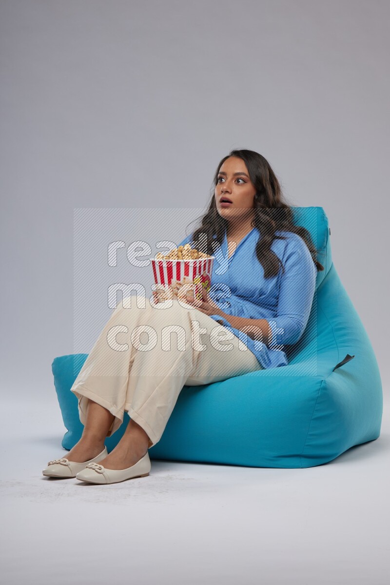 A woman sitting on a blue beanbag and eating popcorn