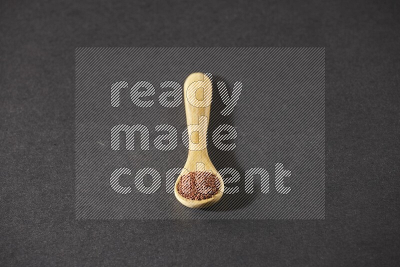 A wooden spoon full of garden cress seeds on a black flooring